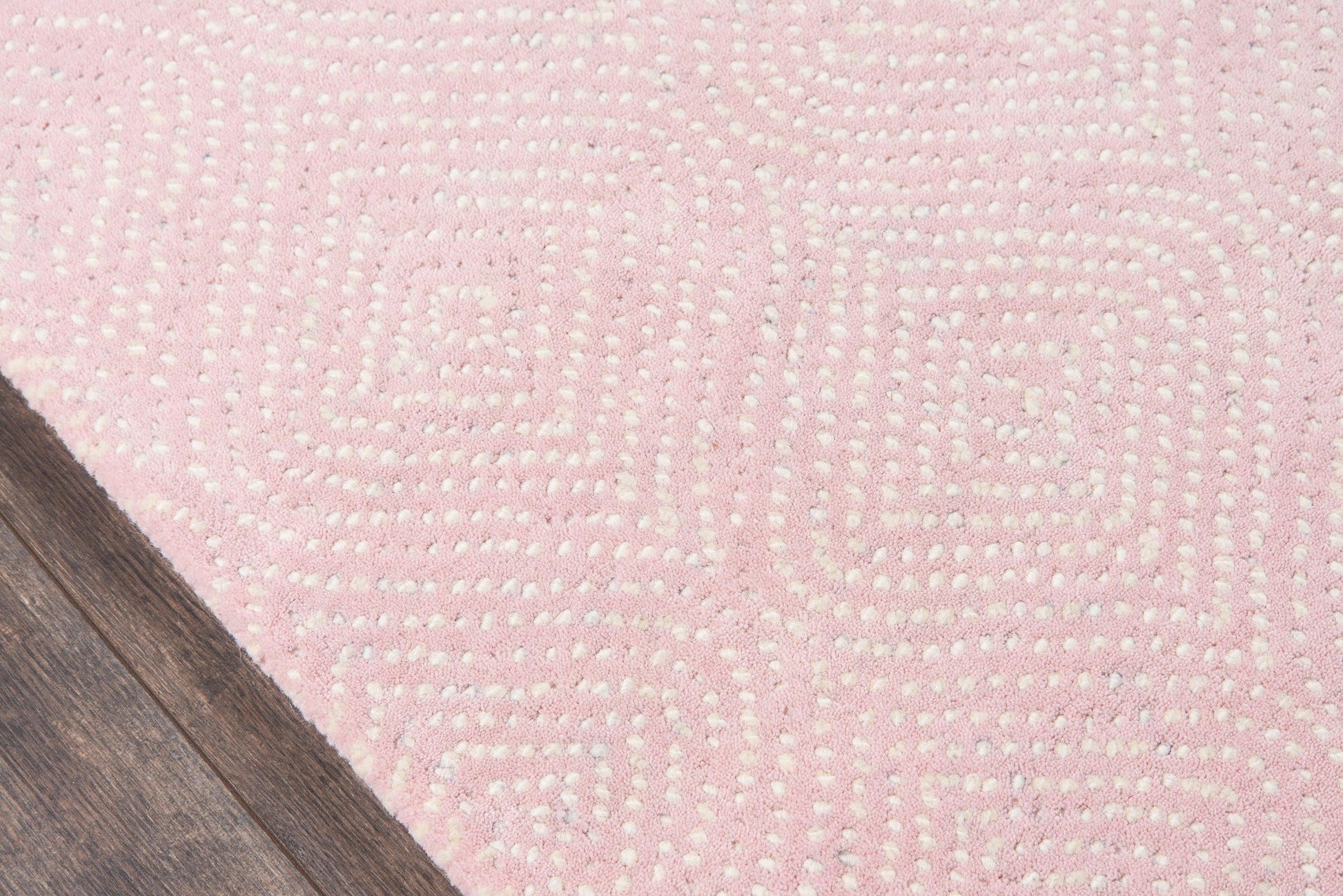 Soft pink area rug with white dotted geometric swirls on dark wood floor corner.