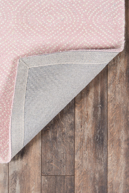 Soft pink rug with white dotted spiral pattern; folded corner reveals gray backing on wood floor.