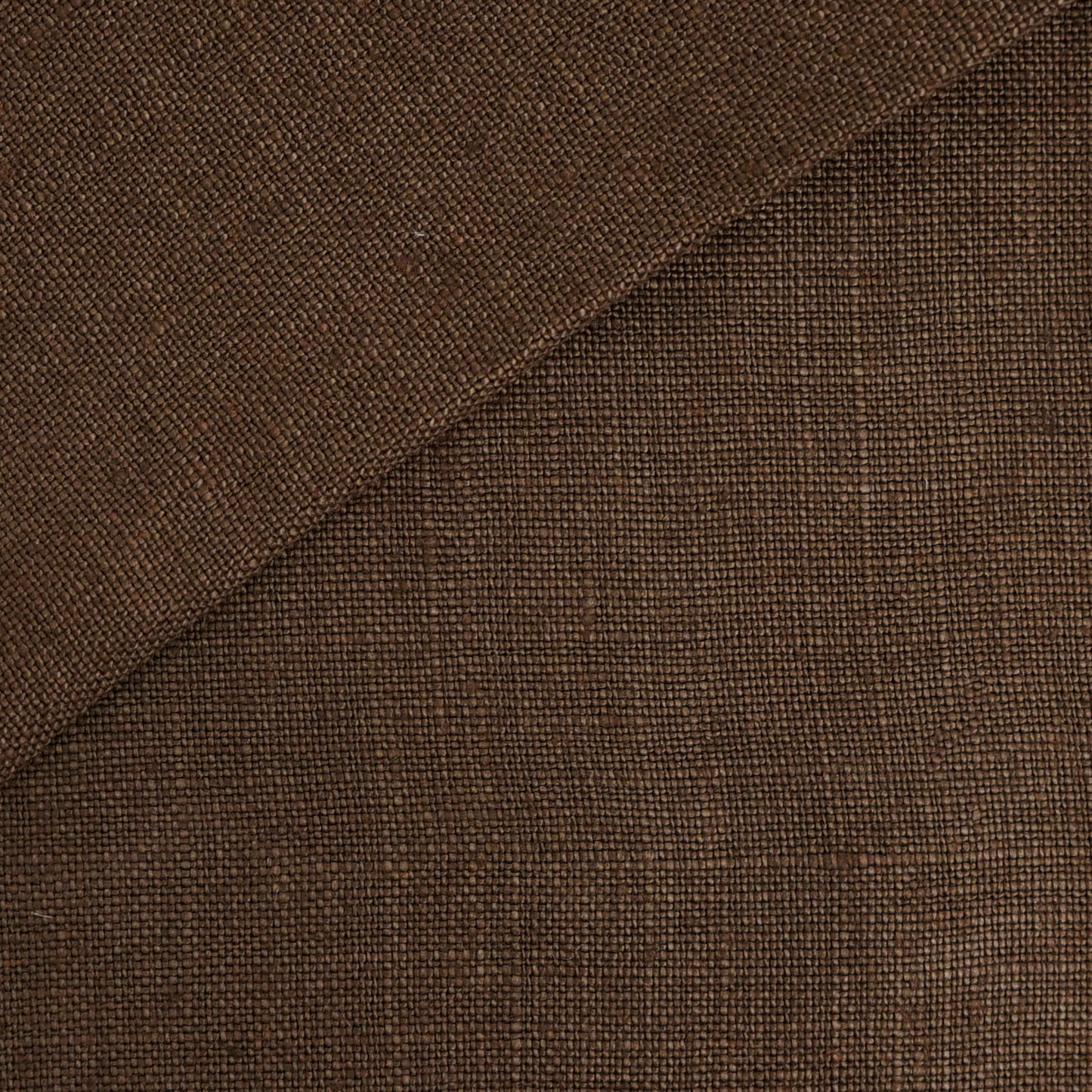 Brown linen fabric close-up with visible texture, diagonal seam, folded edge.