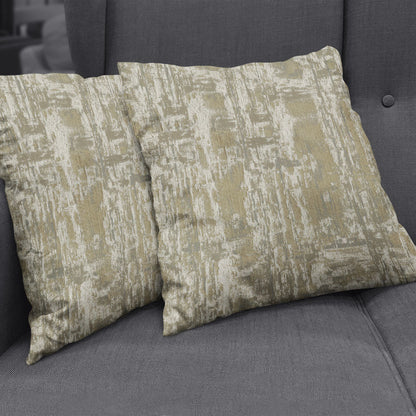 Two square decorative throw pillows with a beige and pale gold hemp abstract pattern on soft chenille/velvet fabric on a gray sofa