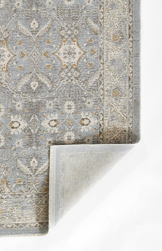 Blue-gray oriental rug with beige and gold accents, ornate pattern; curled corner reveals soft backing.