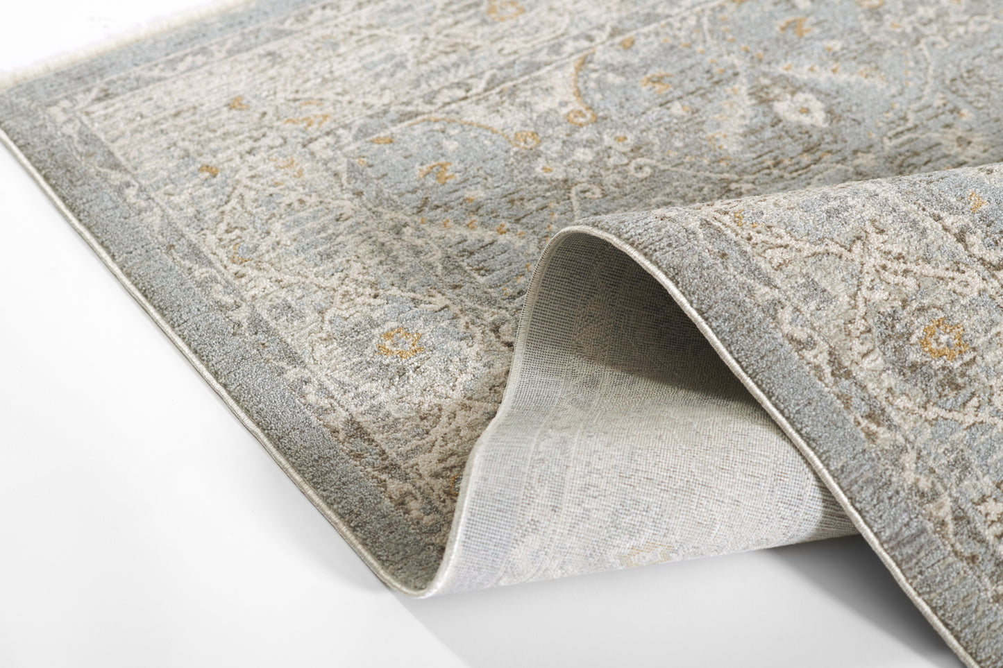 Blue-gray ornate patterned area rug with subtle gold accents, folded corner showing the underside.