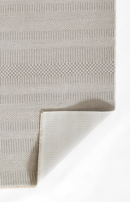 Neutral beige-gray flatwoven rug with chevron and geometric stripe patterns; folded corner reveals lighter underside.