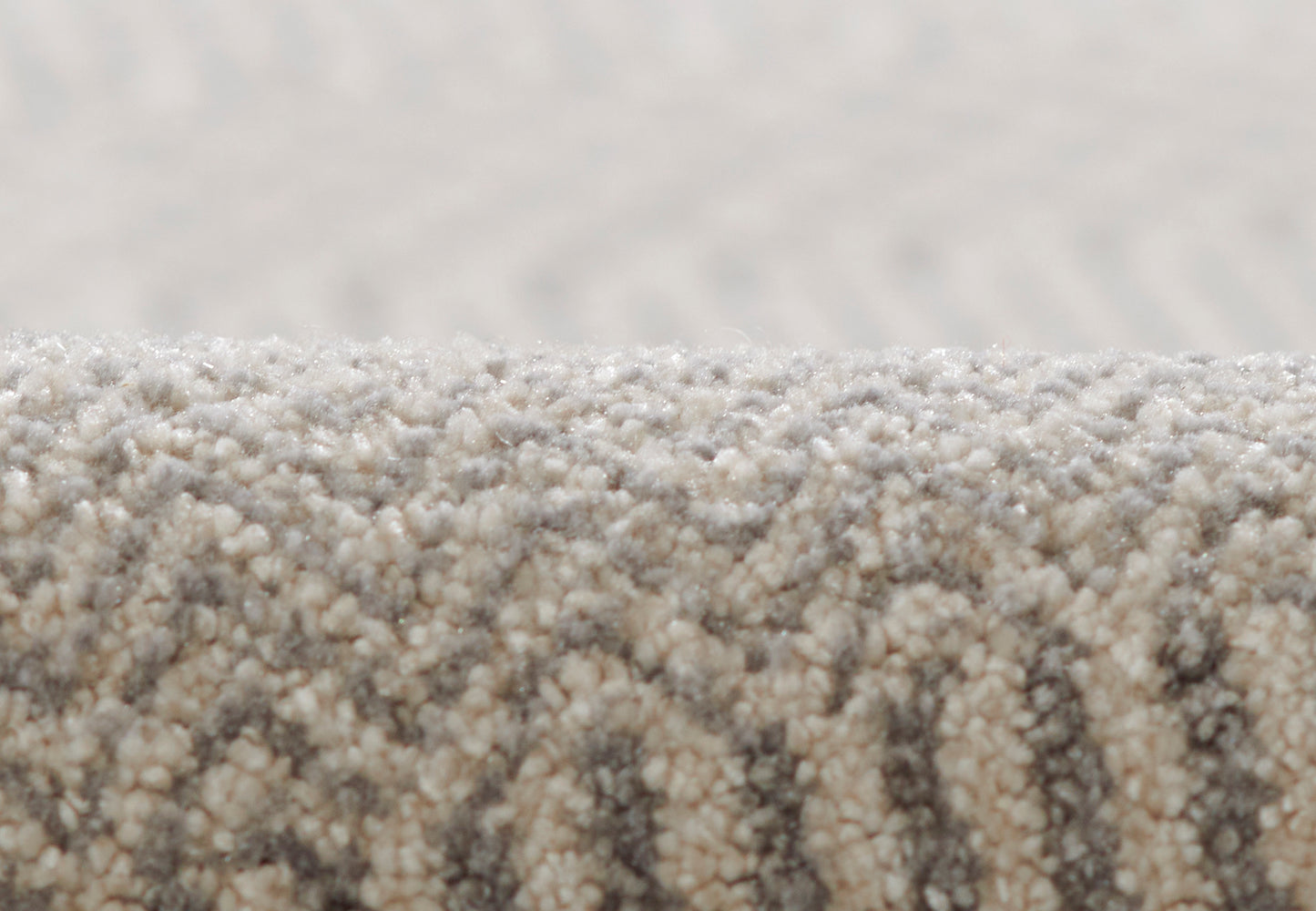 Close-up of beige-grey loop-pile rug with rolled edge and subtle textured pattern.