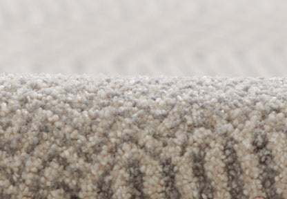 Close-up of beige-grey loop-pile rug with rolled edge and subtle textured pattern.