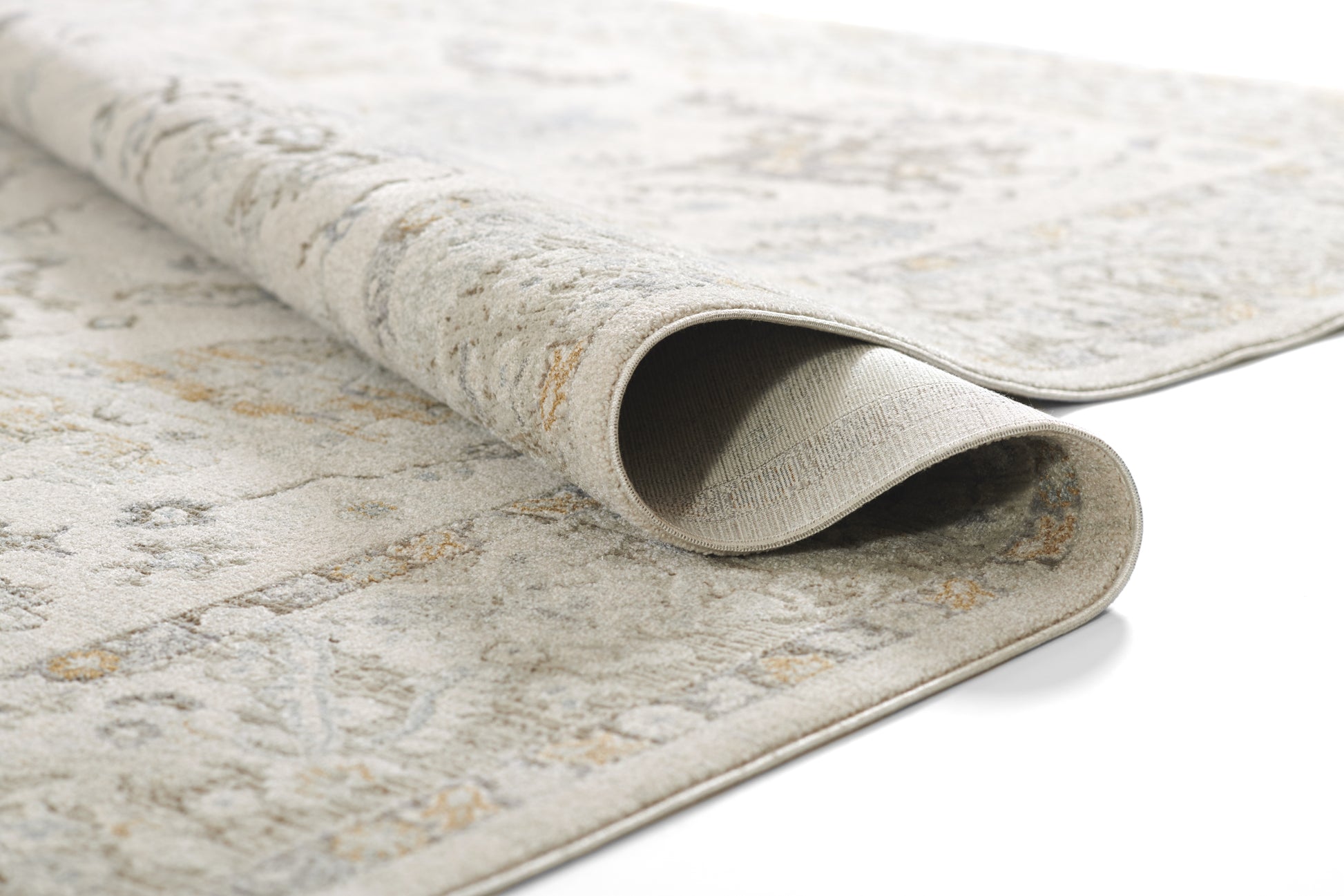Light gray and beige patterned rug, partially rolled, showing soft flat-weave texture and subtle vintage motifs.