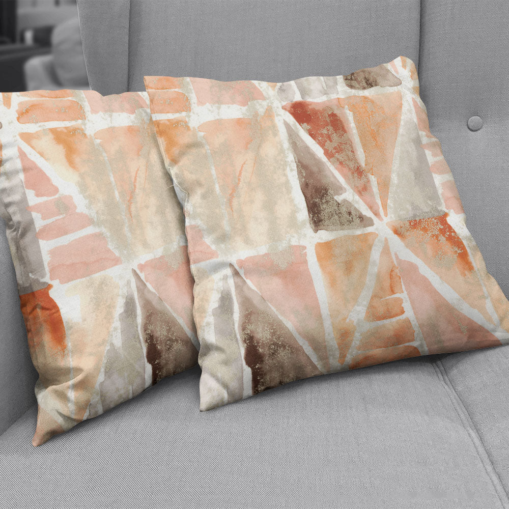 Geometric abstract fabric used for throw pillows in peach, beige and brown on a grey sofa.