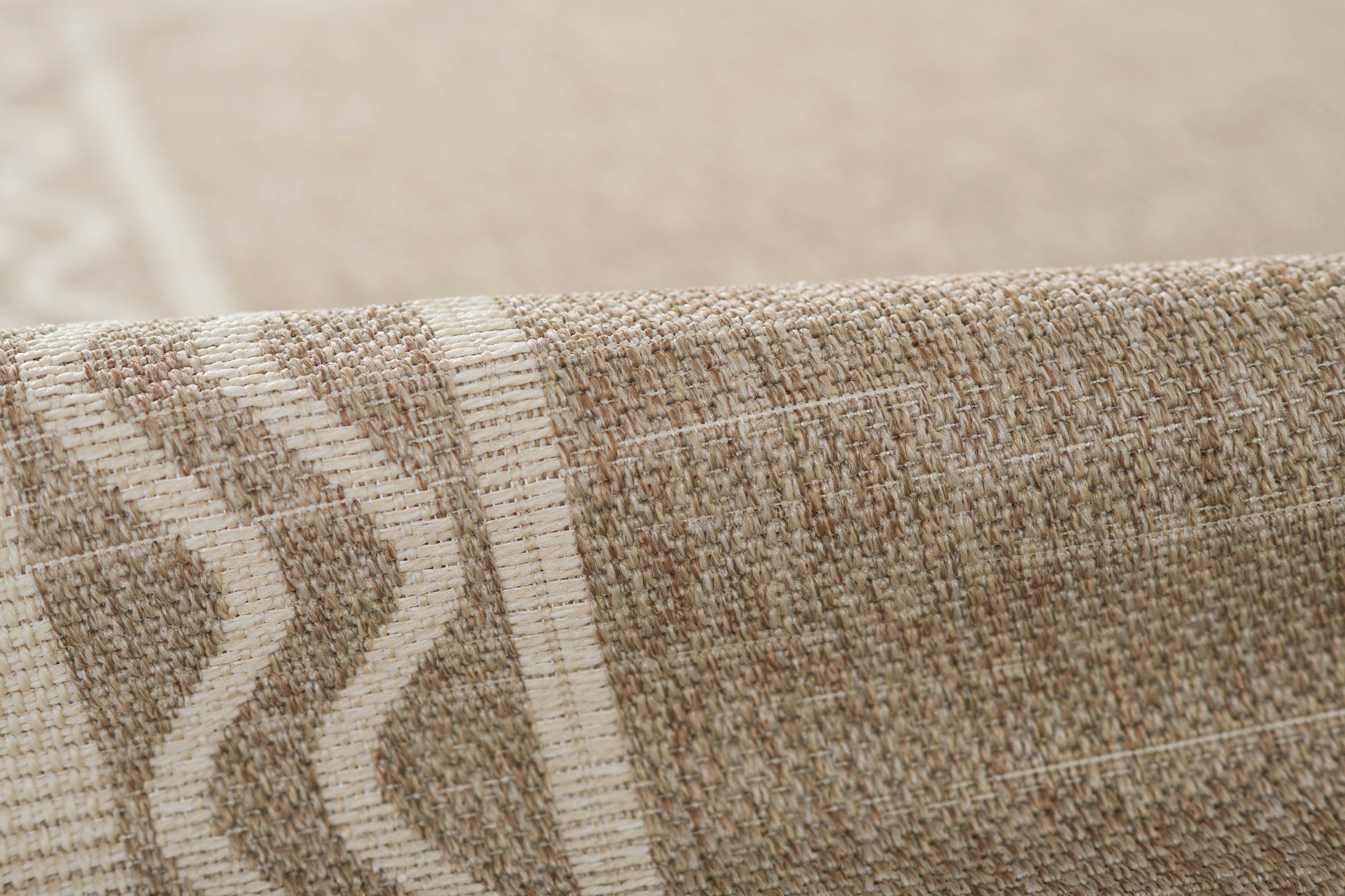 Beige and gray woven rug close-up with chunky fibers and a geometric chevron border.