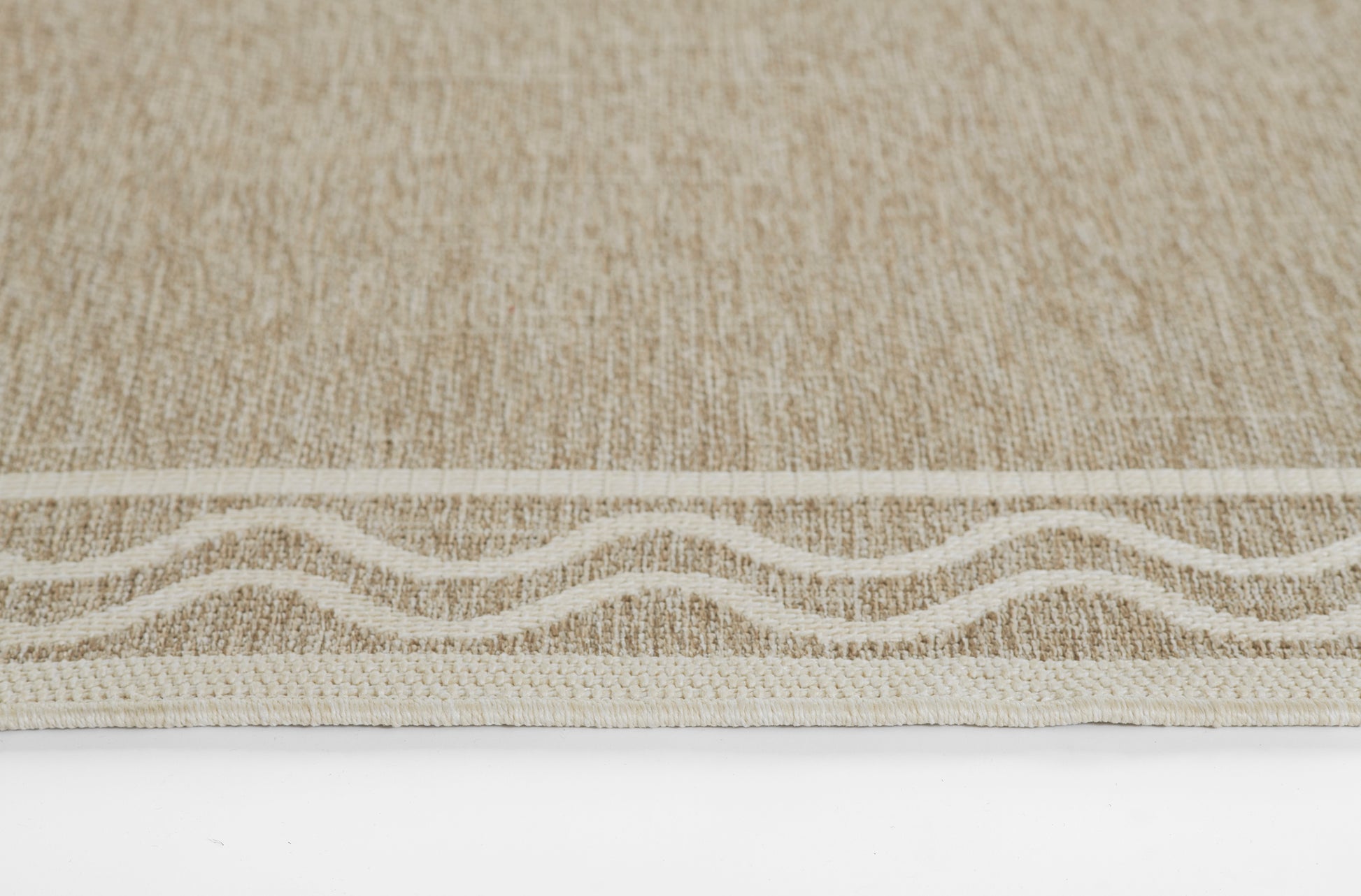 Beige woven rug with subtle texture and cream wavy border along the edge; contemporary coastal style.