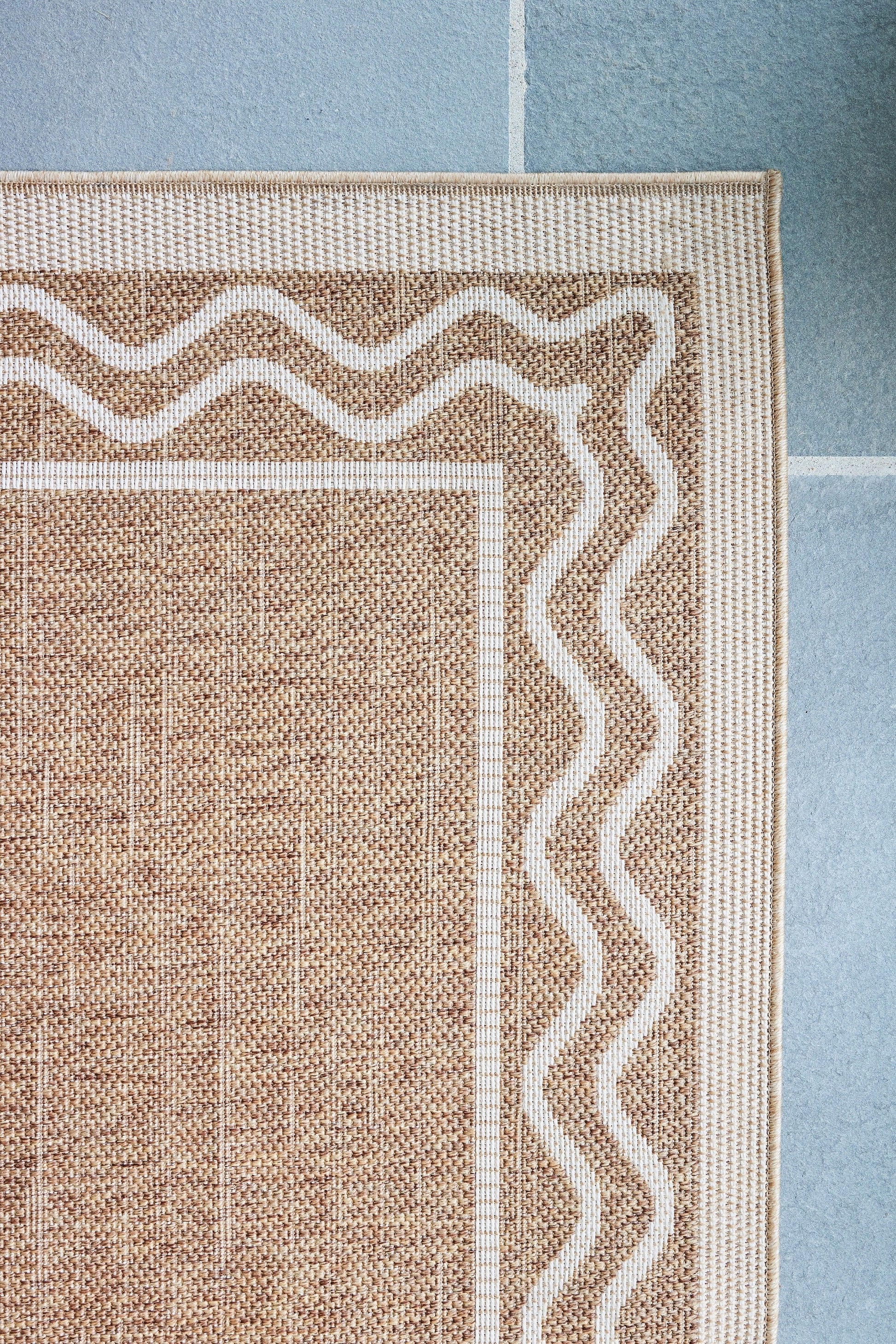 Natural beige woven rug with white wavy border and tan center, on blue tile floor