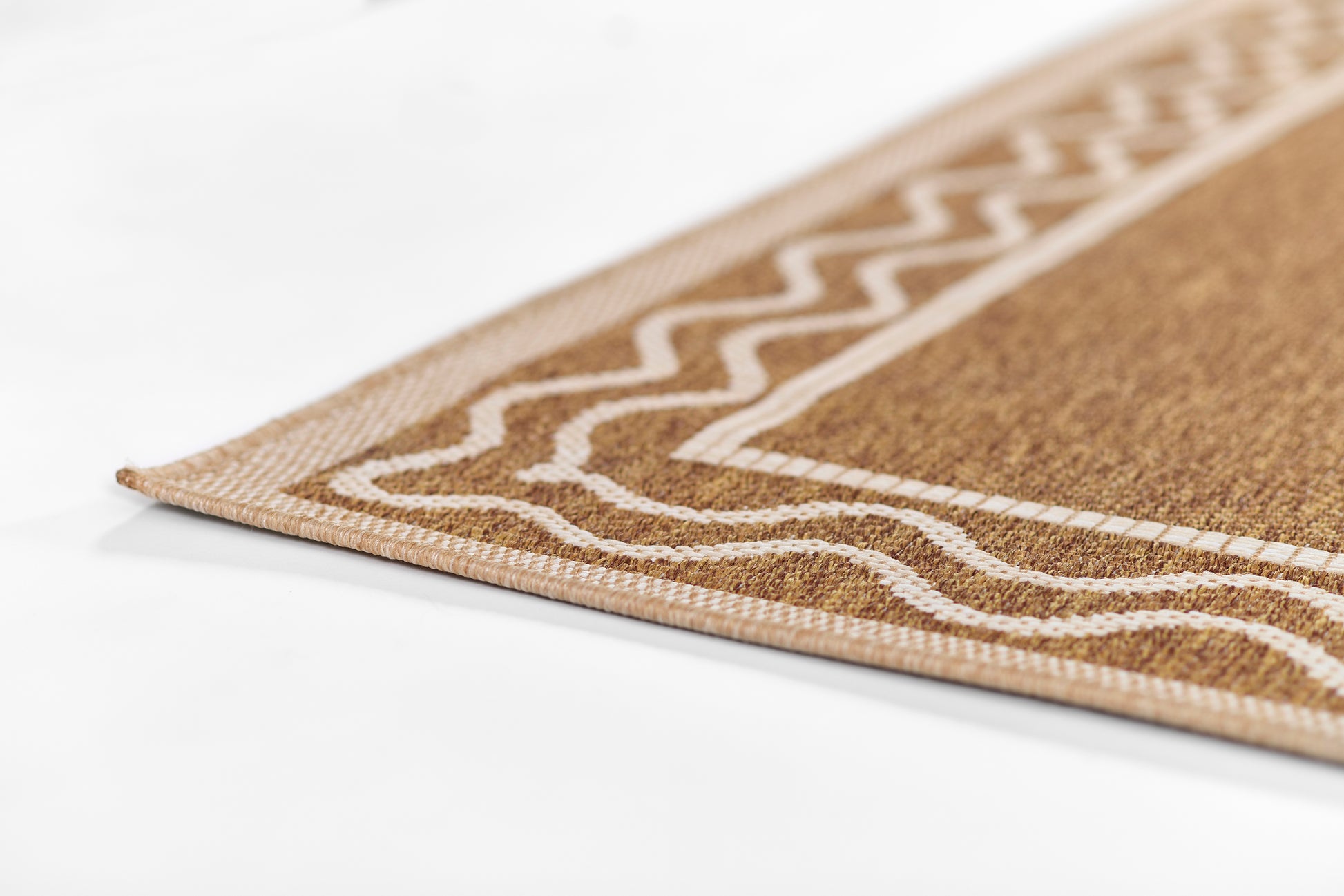 Natural brown woven rug corner with white geometric border; tan tones and chevron pattern.