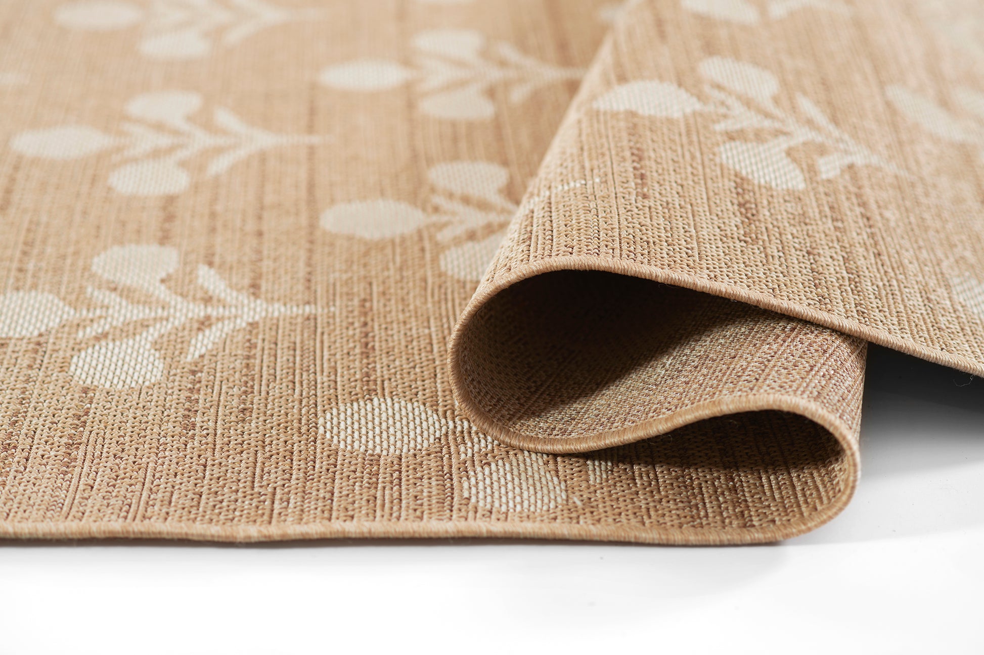 Beige jute rug with white botanical pattern, folded corner reveals natural woven texture.