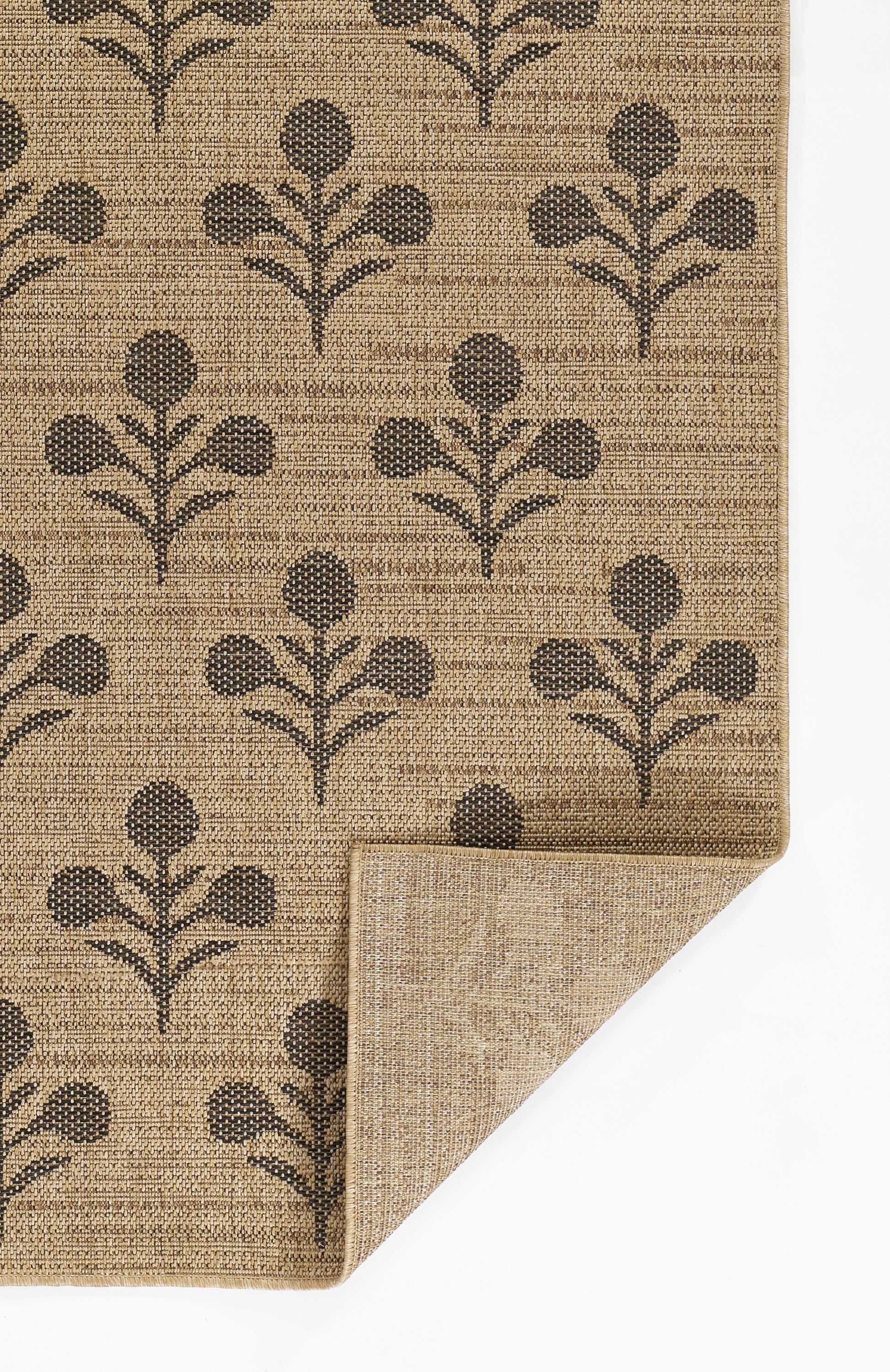 Beige woven rug with dark brown botanical tree-pattern; natural fiber texture, folded corner visible.