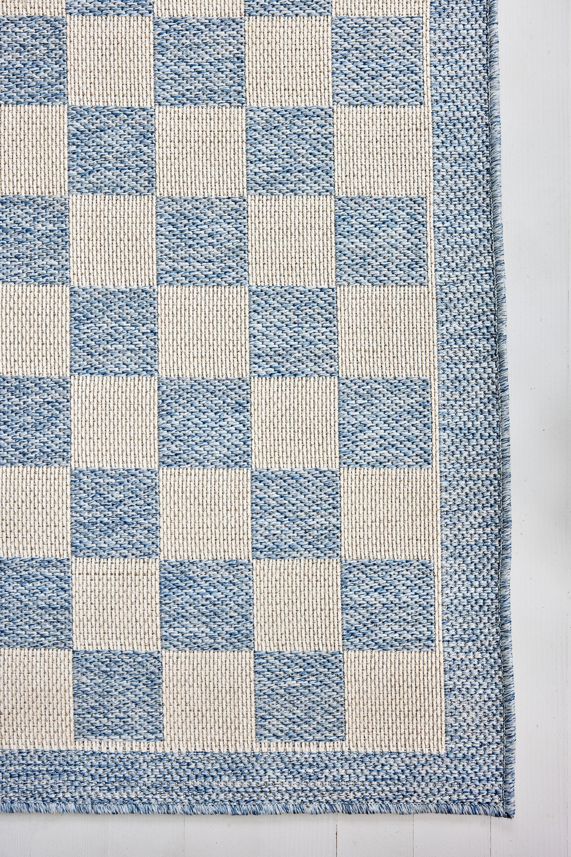 Blue and ivory checkerboard woven rug with a textured surface and blue border.
