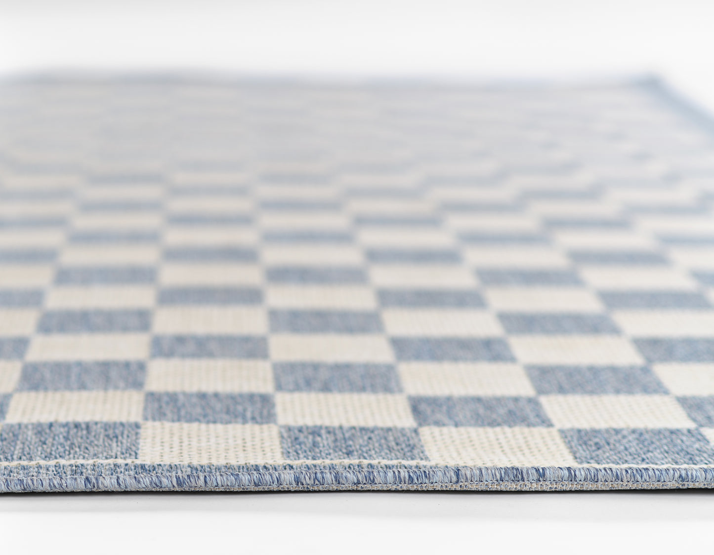 Blue and white checkerboard flatwoven rug with visible woven texture and bound edge.