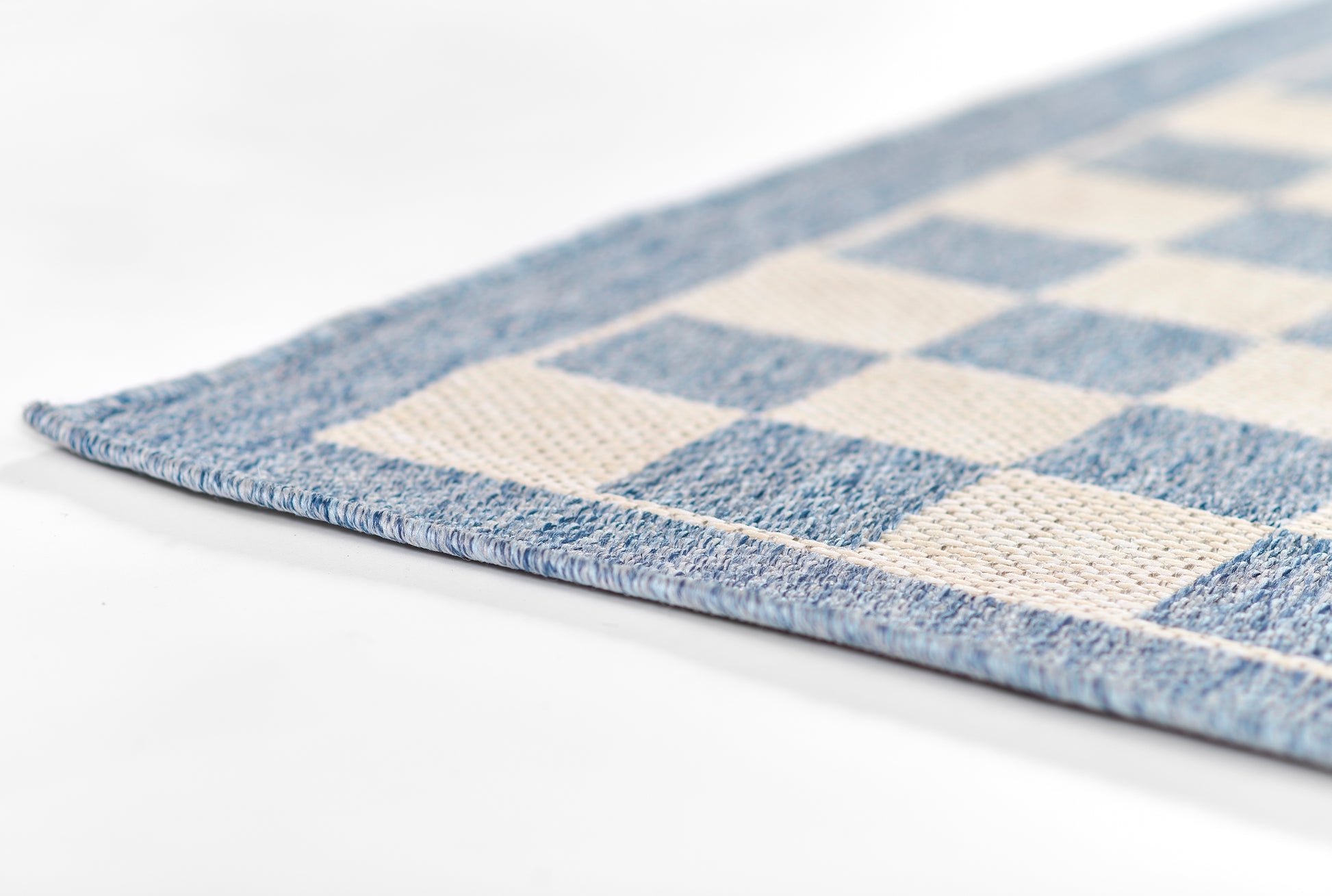 Blue & cream checkerboard rug, woven texture with blue border, close-up corner view.