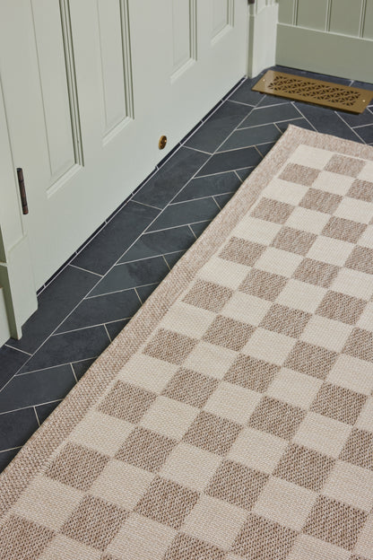 Beige & cream checkerboard rug runner on dark slate floor beside a mint-green door.