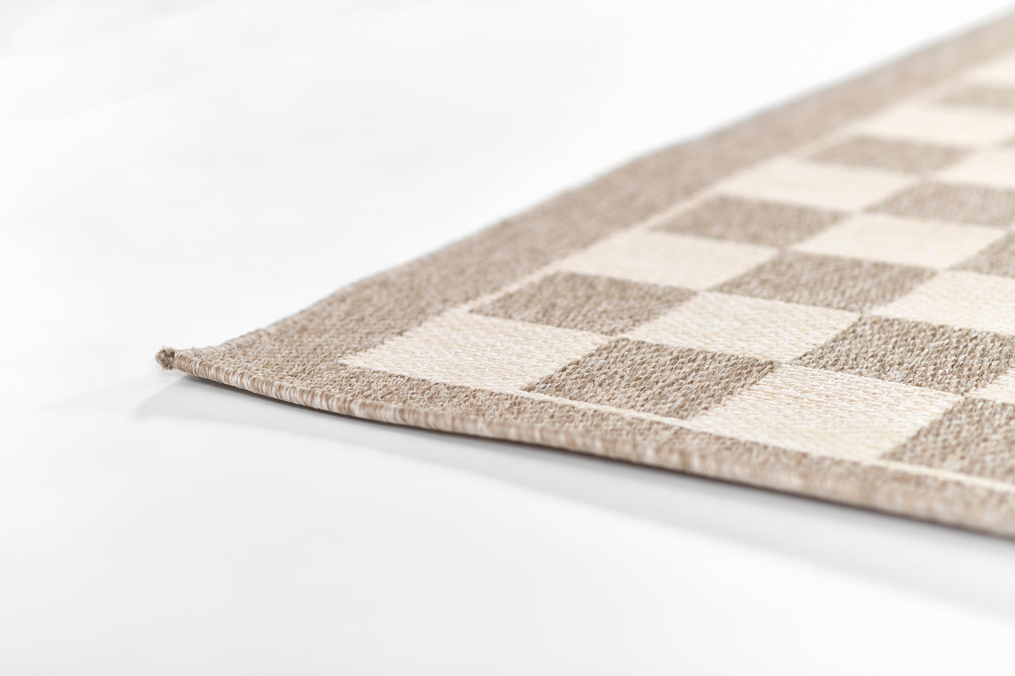 Beige and tan checkerboard rug corner, woven textile with a neutral home decor look.