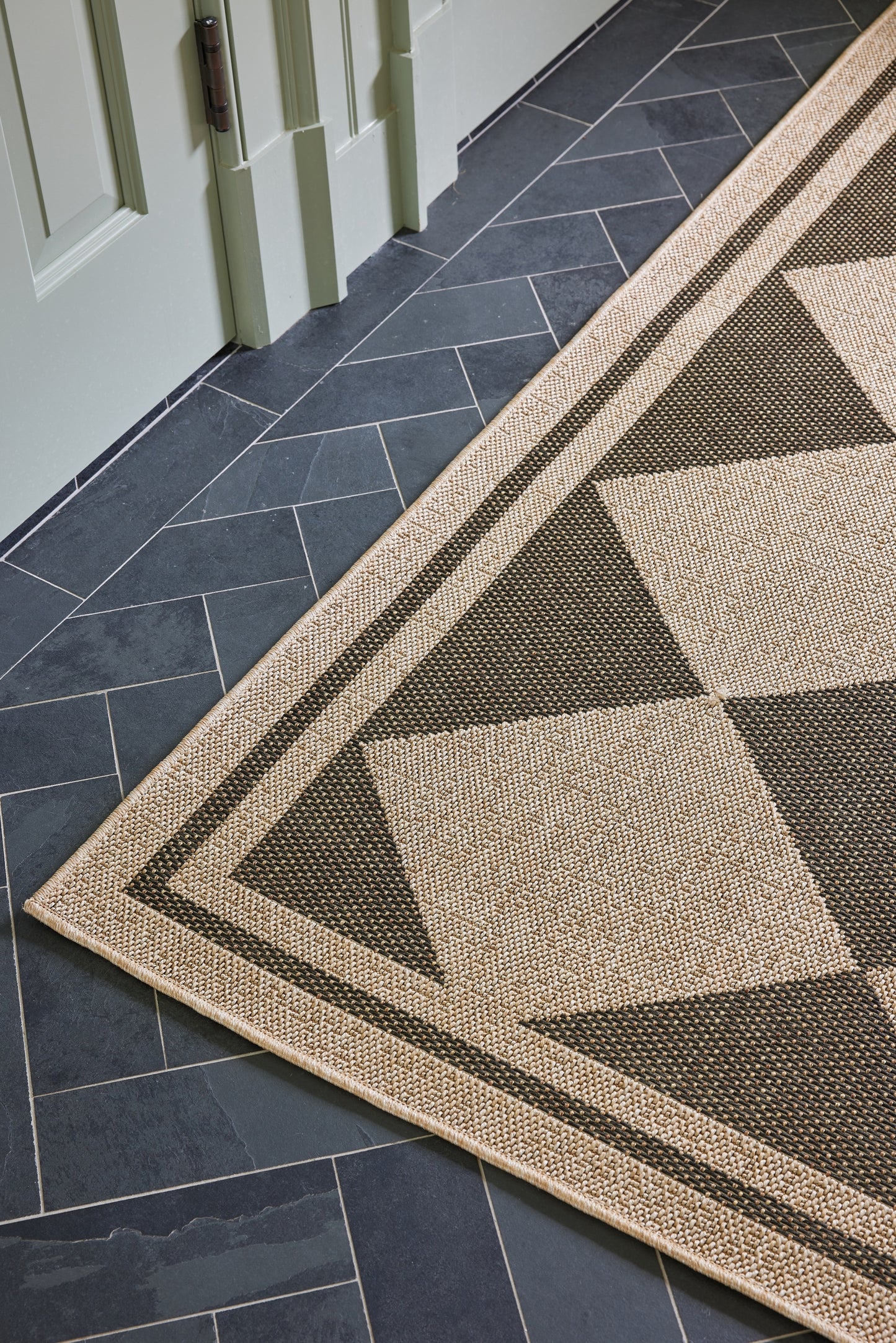 Geometric beige and dark brown triangle runner with a framed border on dark tile floor beside a pale-green door.
