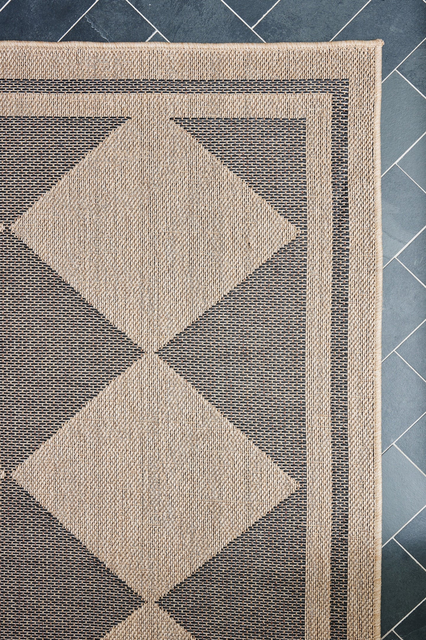 Woven rug with two large beige diamonds on a charcoal gray grid, beige border and geometric frame.
