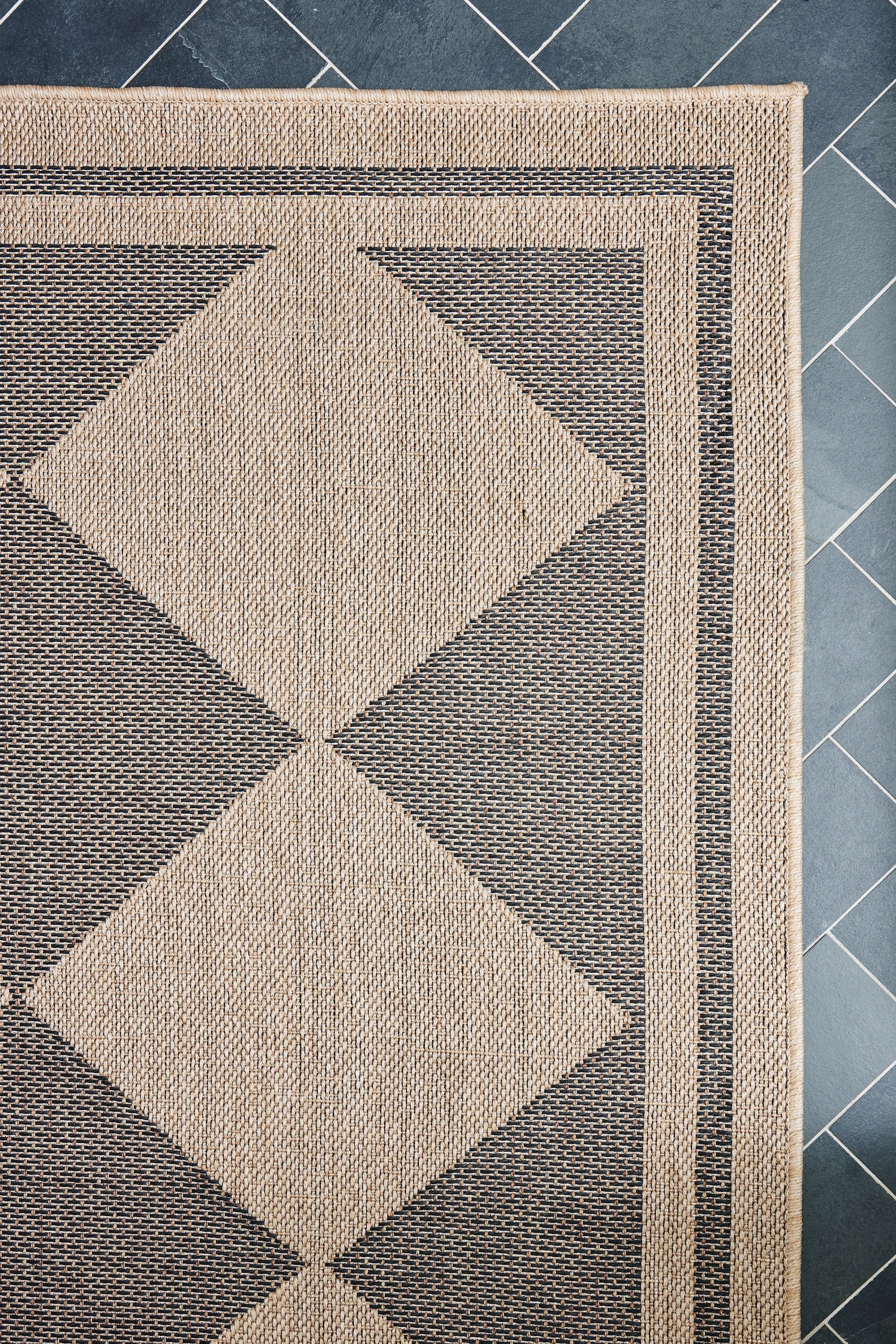 Beige and charcoal woven area rug with large diamond motifs, fringed border, modern geometric design.