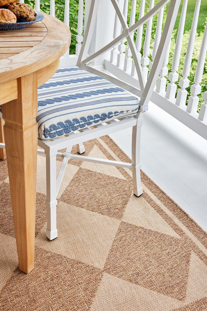 White metal chair with blue striped cushion beside a round wooden table on a beige diamond-pattern porch rug