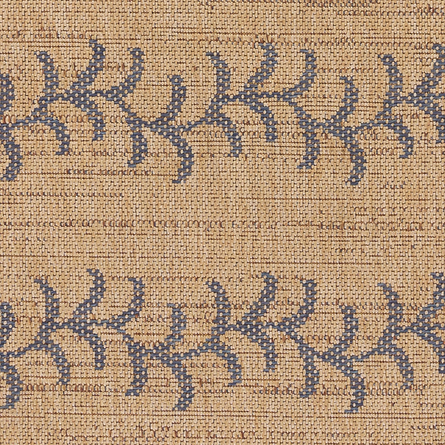 Beige jute rug with repeating navy blue frond pattern; natural coarse weave, boho coastal style.
