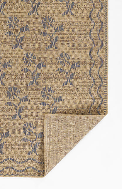 Beige woven jute rug with blue floral vine pattern and a wavy border; folded corner shows the underside.