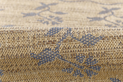 Beige woven rug with blue geometric pattern; textured jute-like fibers, close-up edge.
