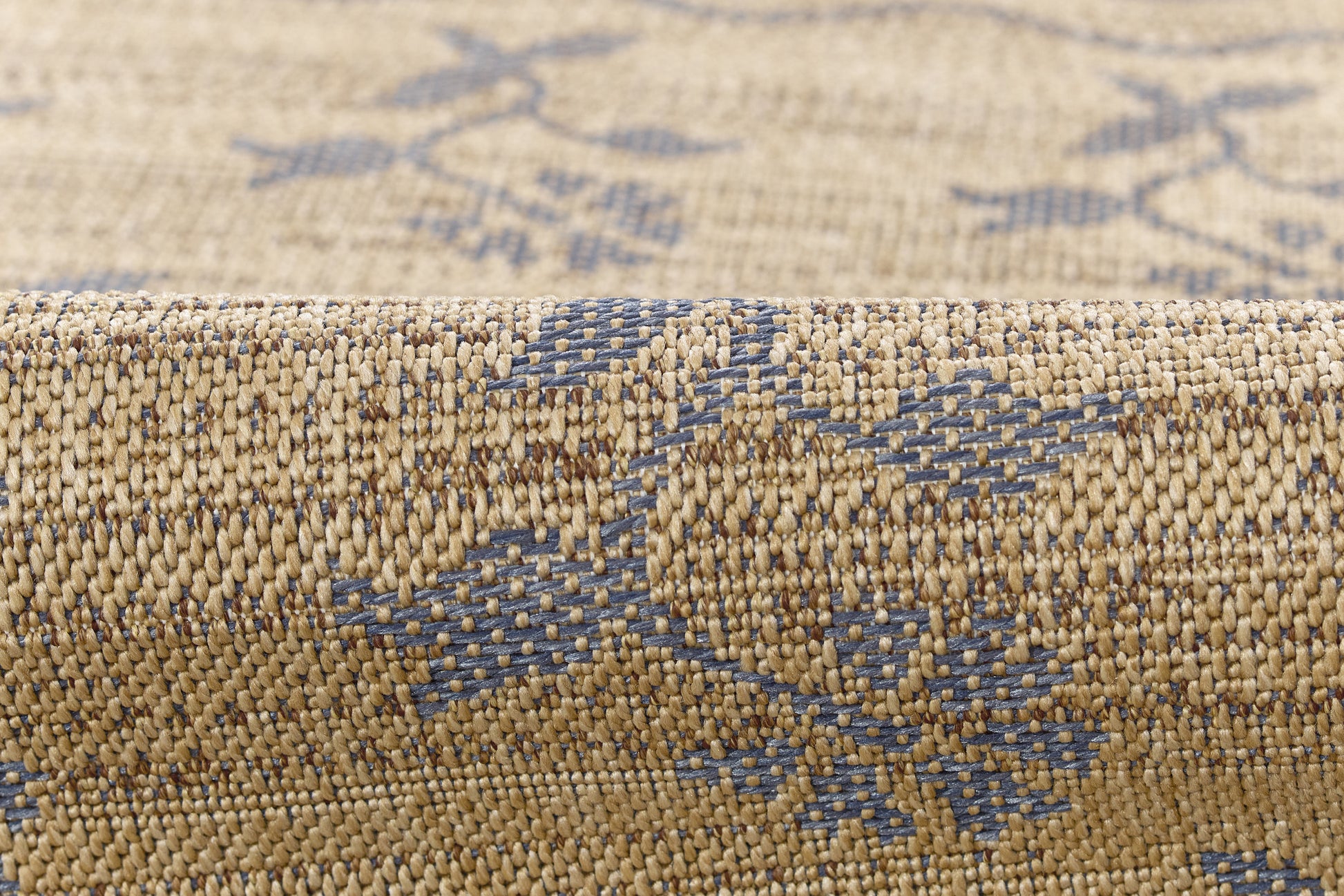 Beige woven rug with blue geometric motif, close-up edge view showing textured fibers.