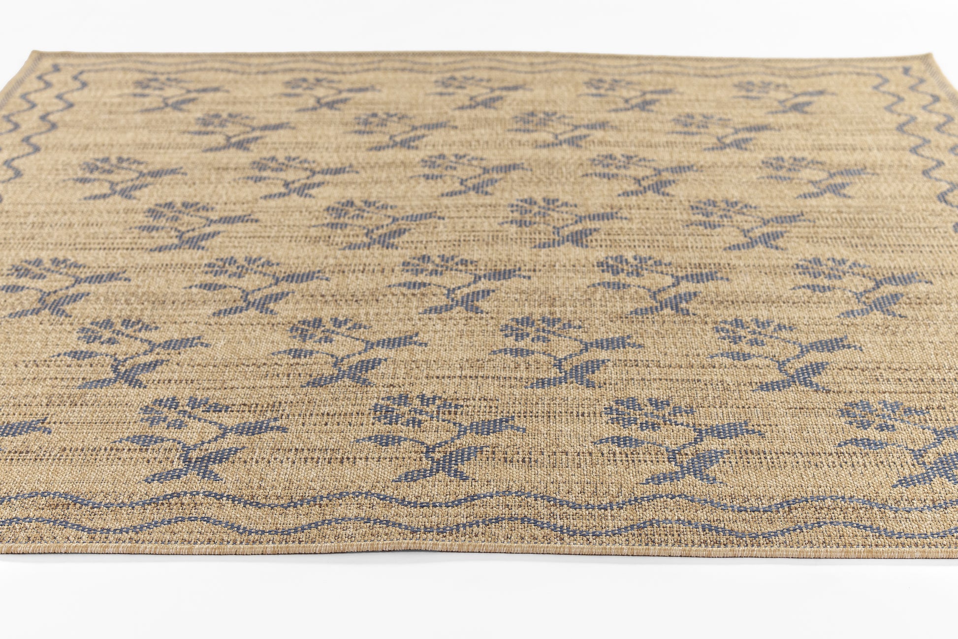 Natural jute rug with blue floral motifs and a wavy border; beige with indigo-blue accents.