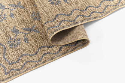 Beige jute rug with blue floral vines and wavy border, thick woven texture, rolled corner.