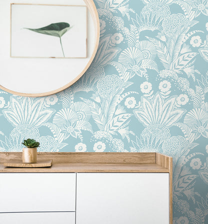 Round wooden-framed mirror over a light wood and white cabinet with a small succulent, blue botanical wallpaper backdrop.