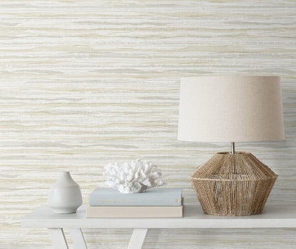 Neutral decor vignette featuring a sisal coastal beige rug, a small ceramic vase, white coral, stacked books, & a woven wicker lamp with a beige shade.