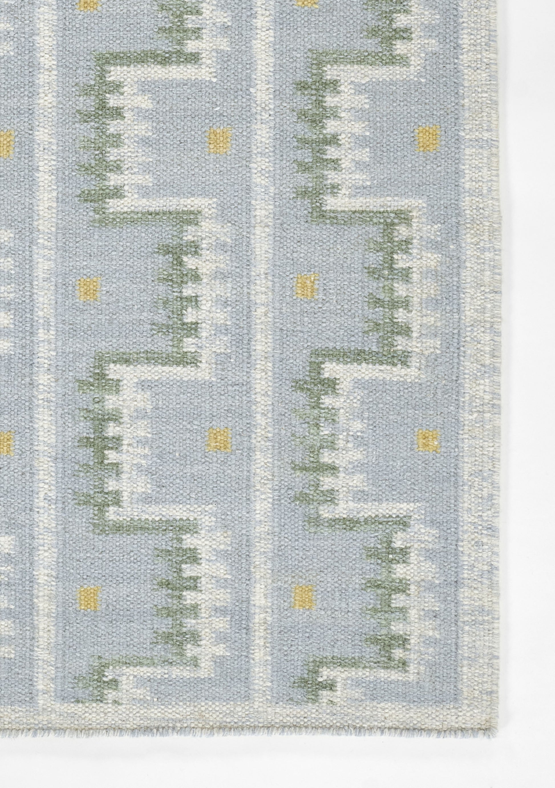 Blue woven rug with white stepped zigzag motif, green accents and small yellow squares; Scandinavian-inspired design.