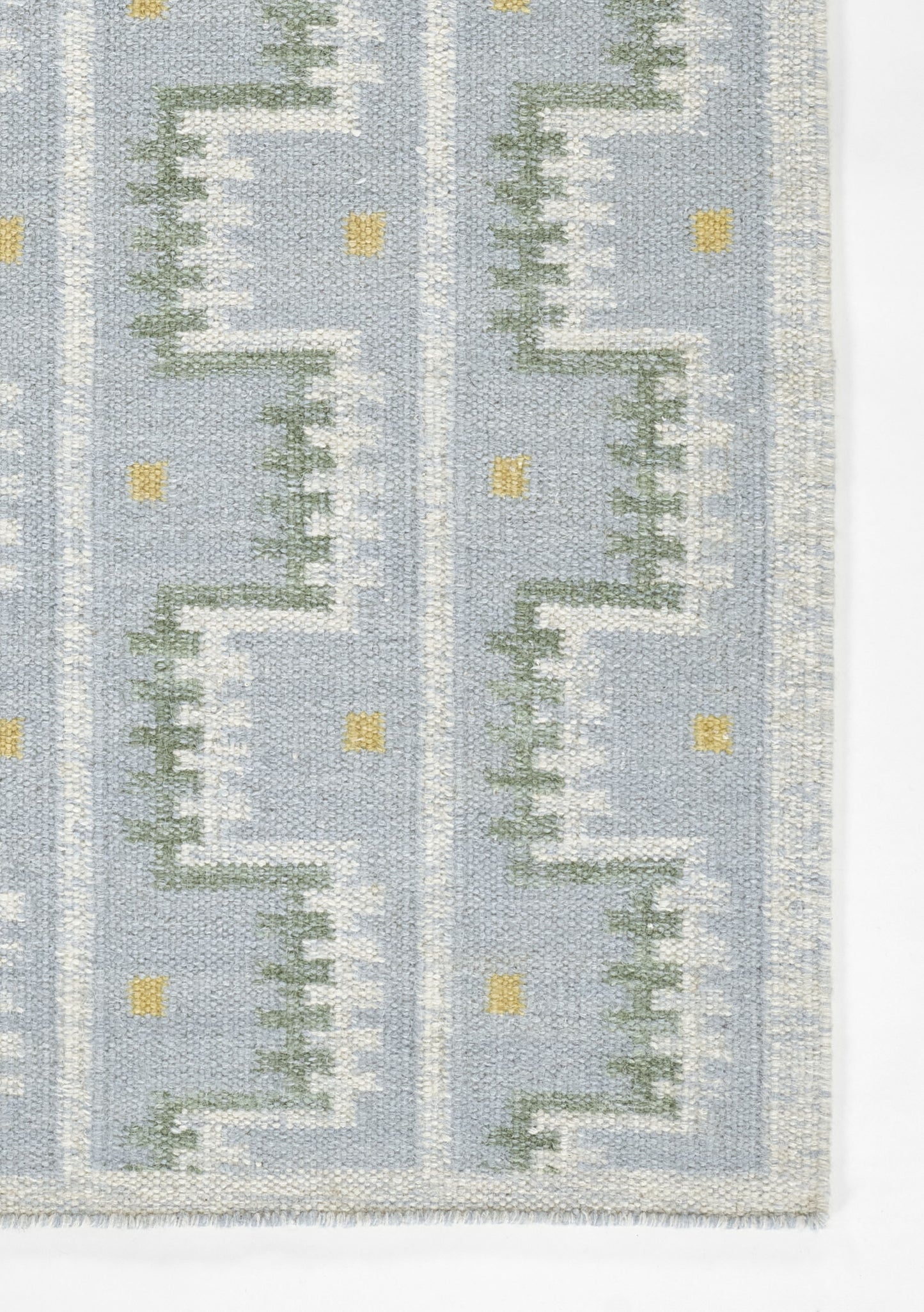 Blue Scandinavian-style rug with white stepped geometric pattern, green accents and small yellow squares.