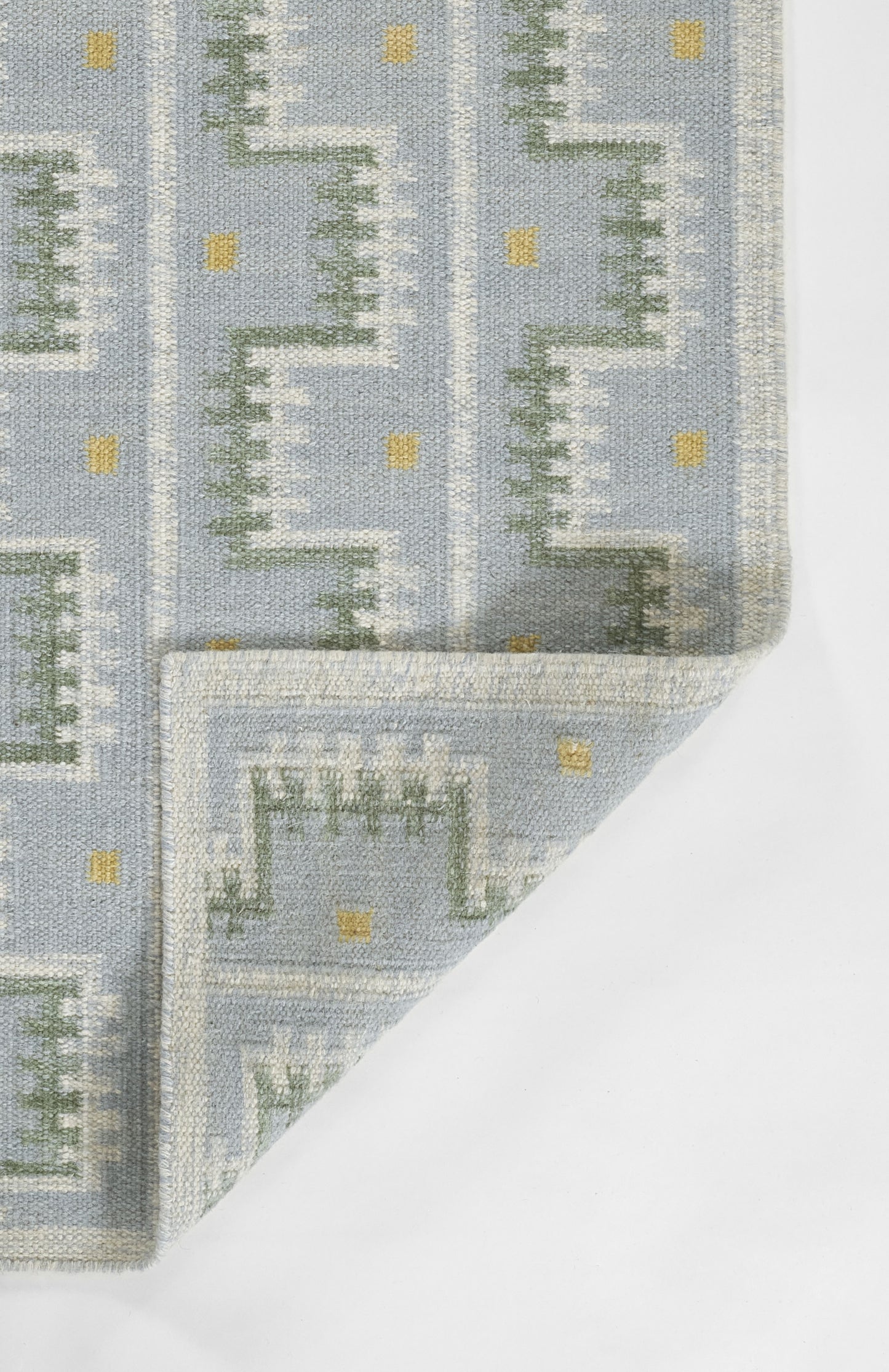 Blue-gray rug with a Nordic-inspired green stepped geometric pattern and small yellow squares; folded corner.