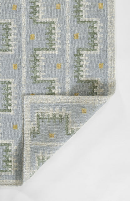 Blue-gray rug with a Nordic-inspired green stepped geometric pattern and small yellow squares; folded corner.