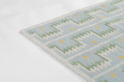 Partial view of a light blue Scandinavian rug with green zigzag motifs and small yellow diamonds.