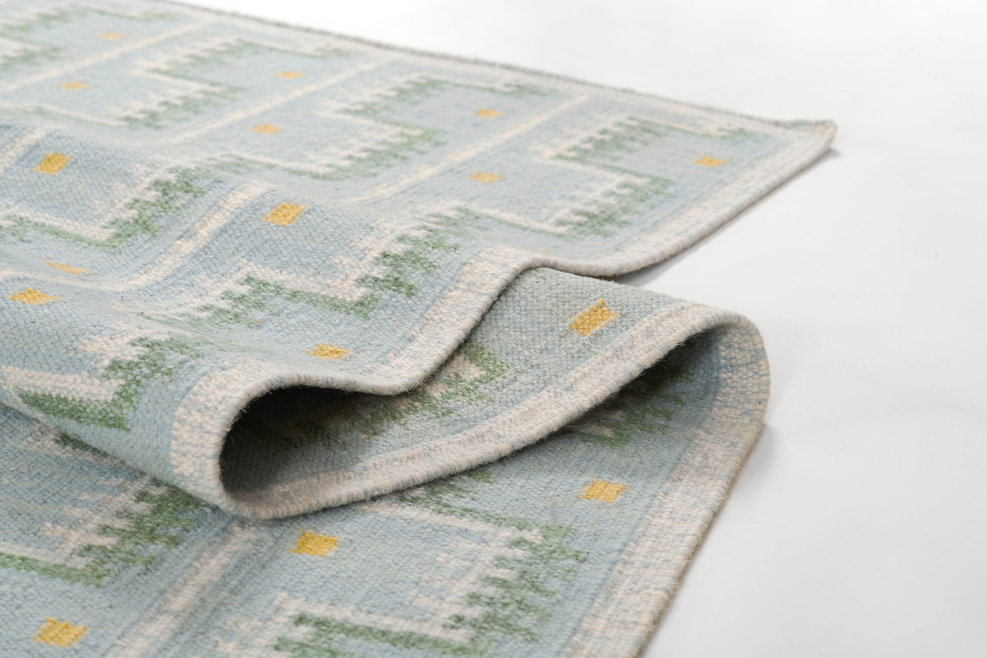 Blue-toned Scandinavian rug with geometric pattern in gray, green, and yellow; folded edge.