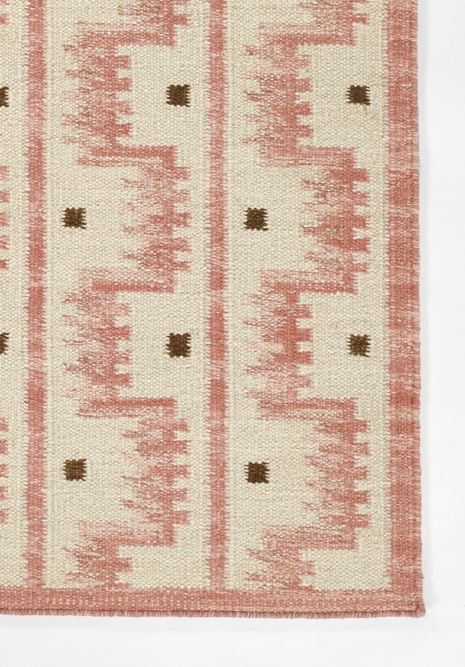 Cream flat-weave rug with dusty pink geometric zigzags and small brown squares; Scandinavian kilim style.