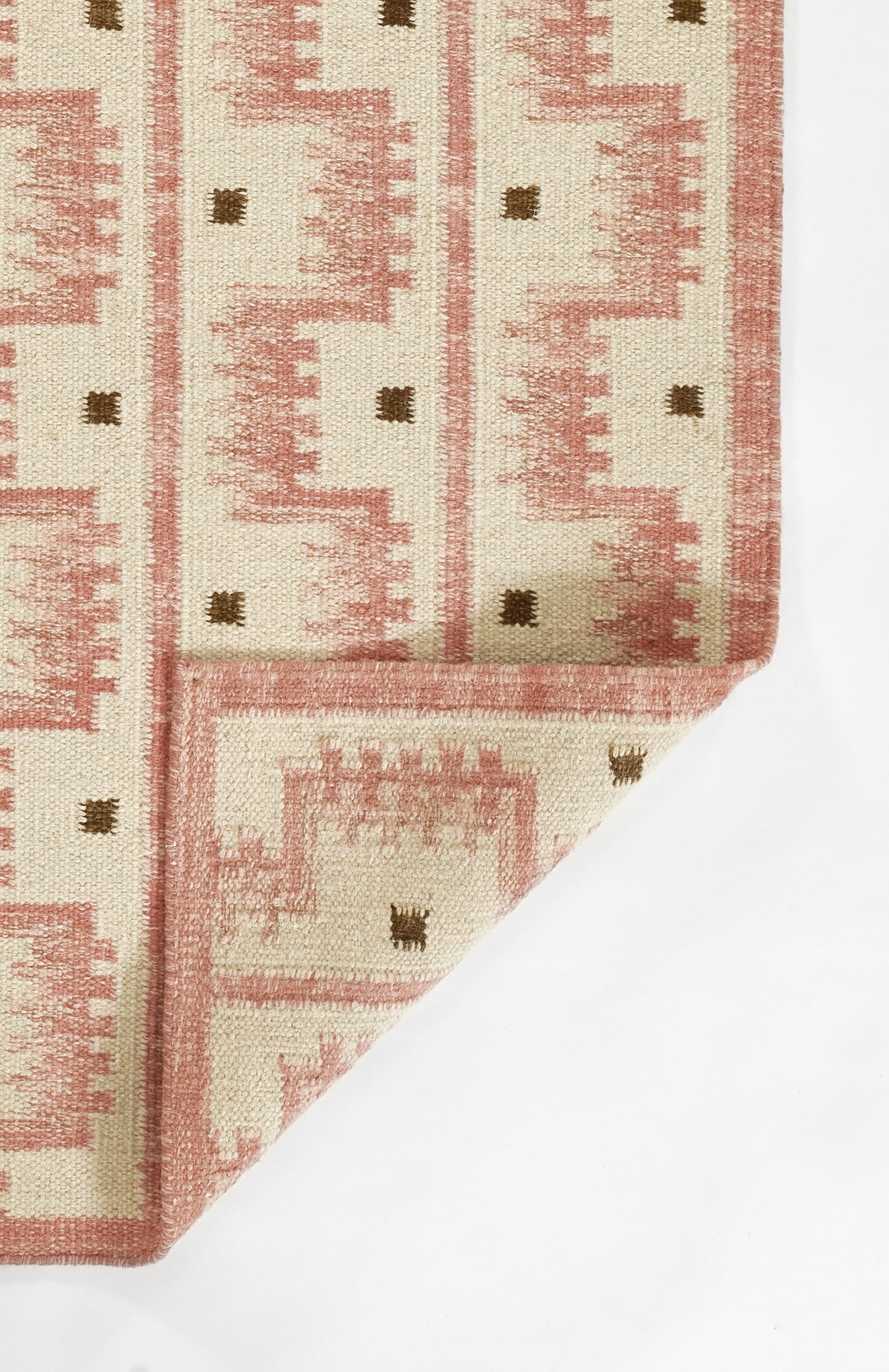 Scandinavian-style woven pink and cream geometric rug with brown dot accents, folded at corner.
