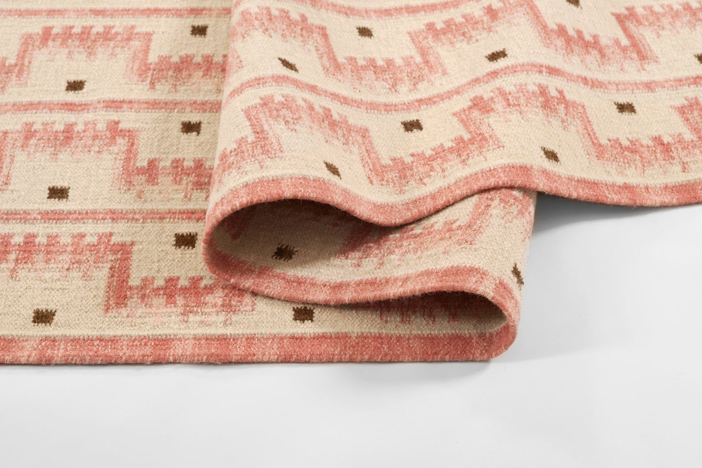 Pink peach woven runner with geometric zigzag pattern and small brown squares, folded to show soft woven edge.