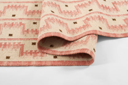 Pink peach woven runner with geometric zigzag pattern and small brown squares, folded to show soft woven edge.