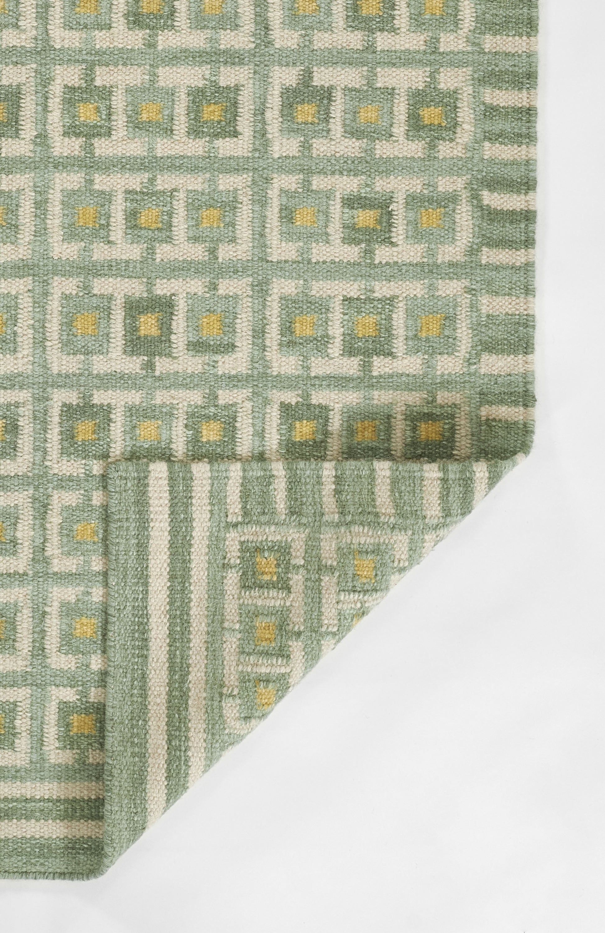 Green and grey woven rug with repeating square motif and yellow centers; folded corner, Scandinavian style.