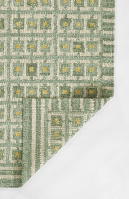 Green and grey woven rug with repeating square motif and yellow centers; folded corner, Scandinavian style.