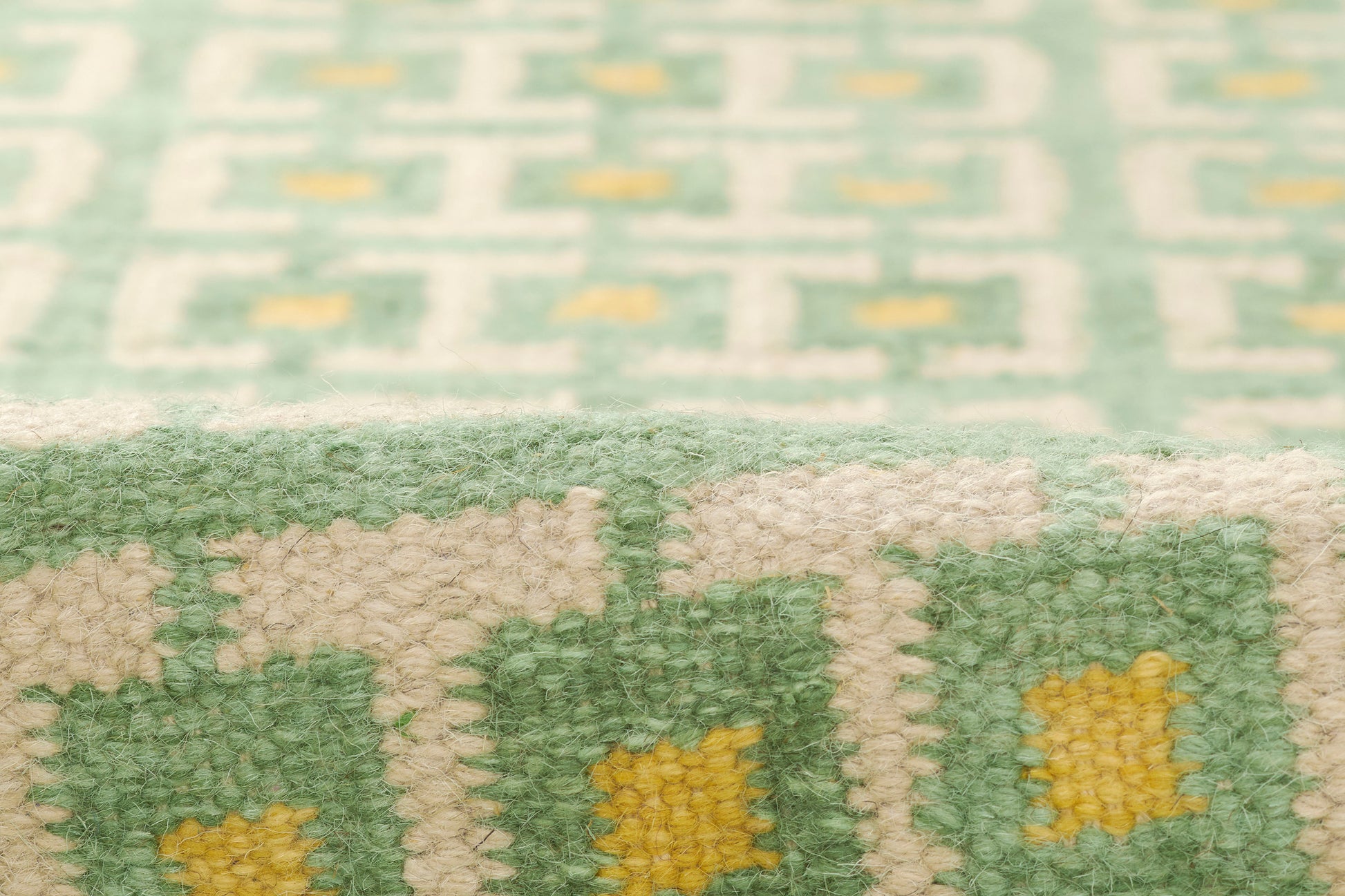 Close-up of a green and white Scandinavian-style geometric rug with small yellow accent squares, woven pile.