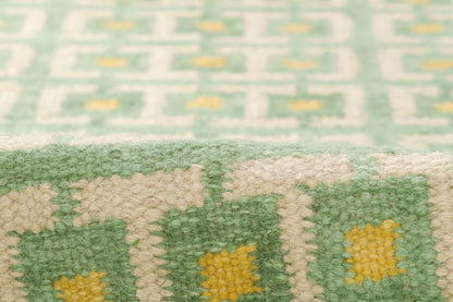 Close-up of a green and cream woven rug with yellow geometric blocks in a Scandinavian-inspired pattern.