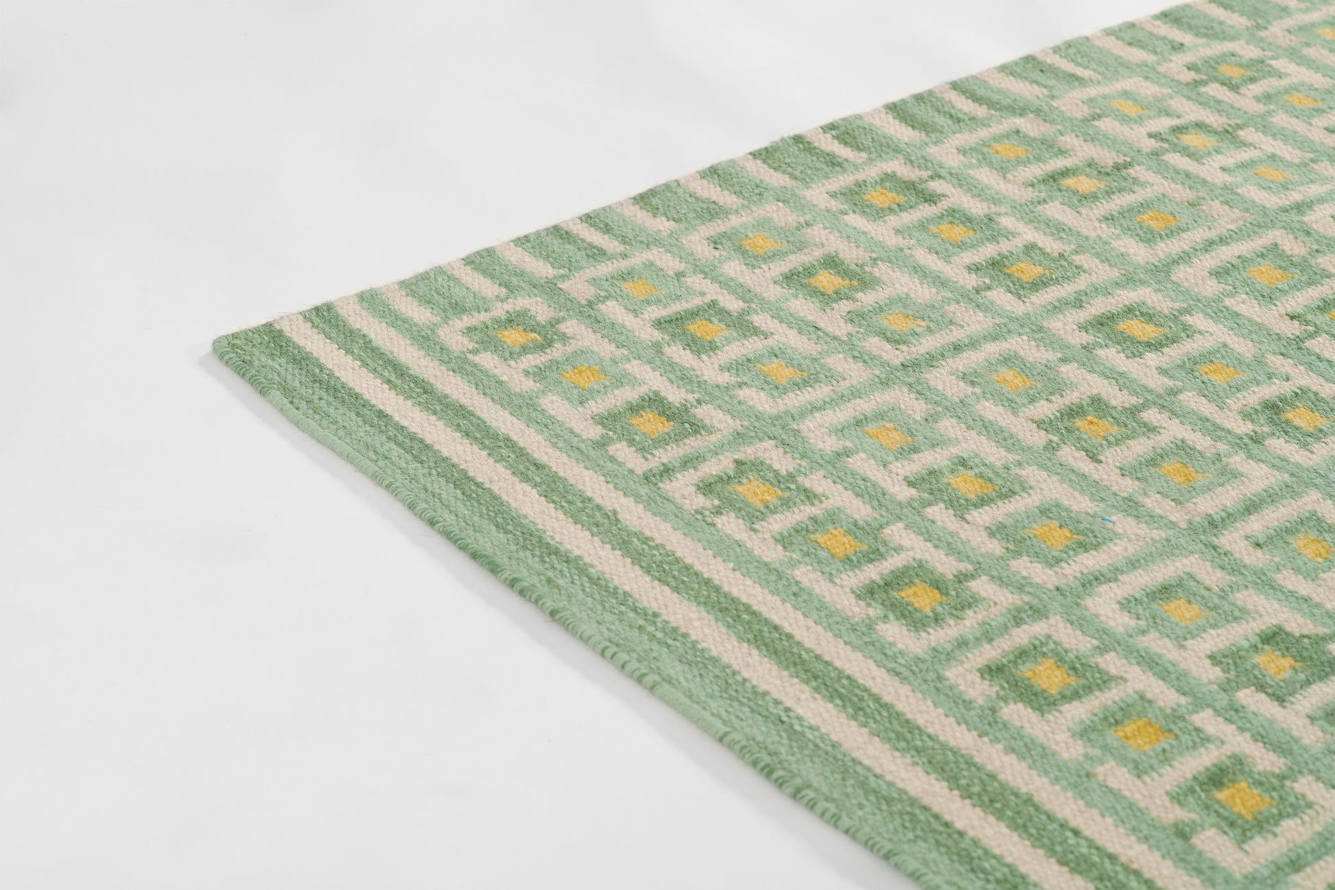 Soft woven mint green and white rug with a geometric lattice pattern and yellow diamond accents, bordered with stripes.