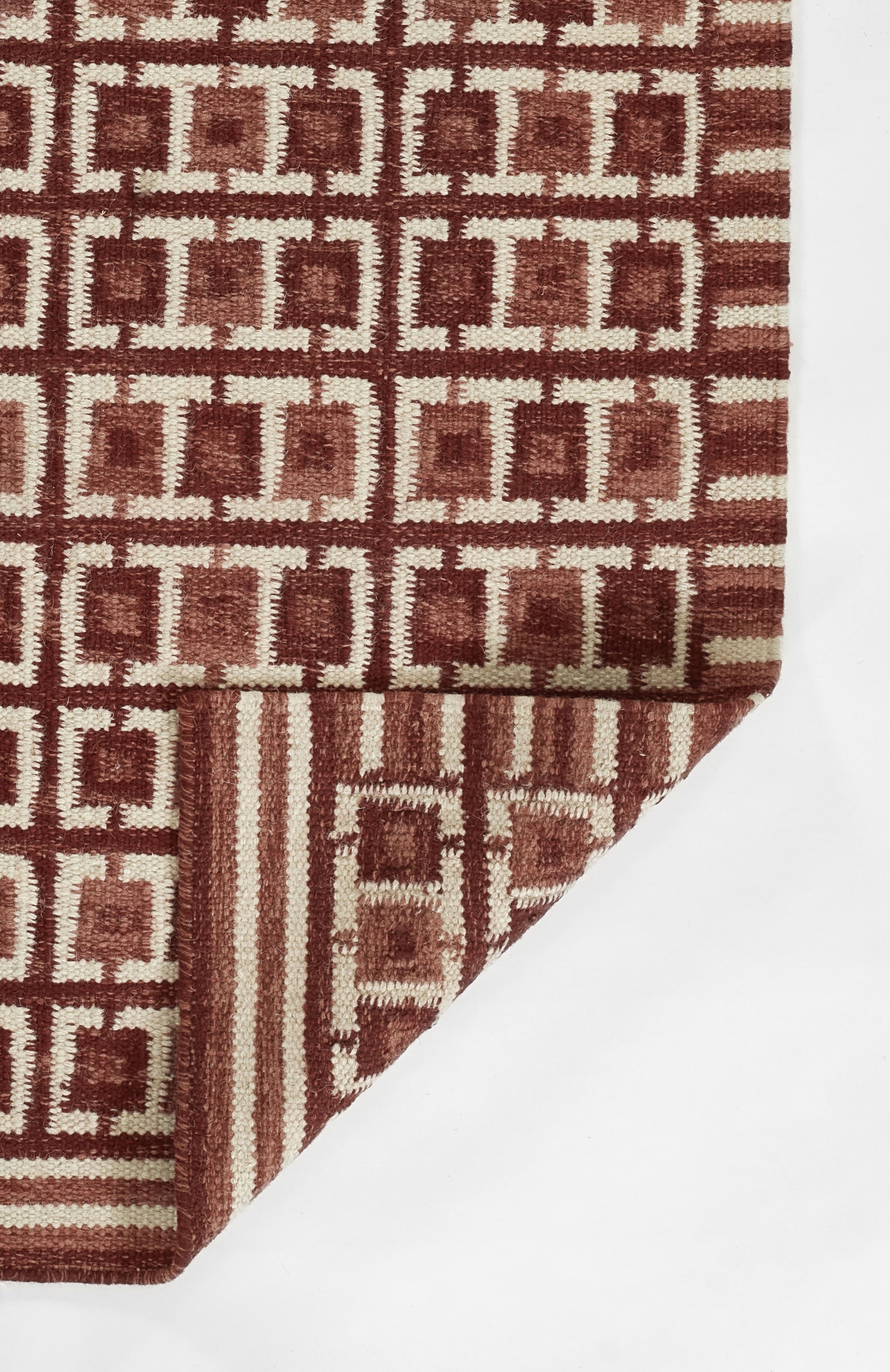 Red-brown Scandinavian geometric rug with square grid motif; woven textile with folded corner showing edge detail.